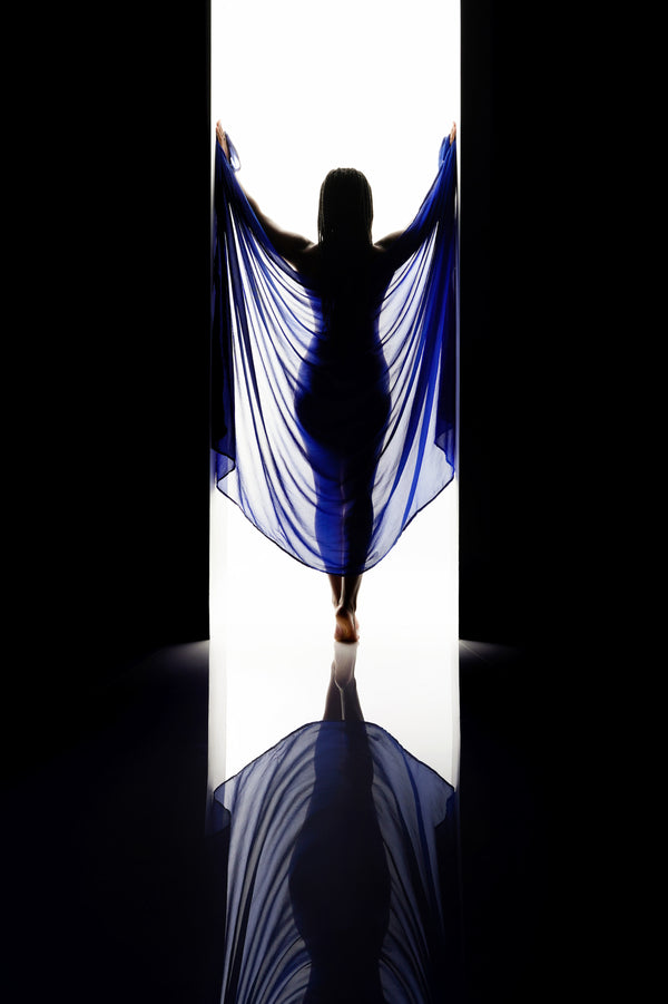 Dramatic window-lit silhouette from the Self-Love Collection, individual with blue fabric, creating a dynamic reflection