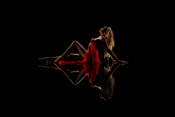 Low-key portrait from the Self-Love Collection, individual in striking red fabric with a reflective pose on a dark background, exuding strength and vitality