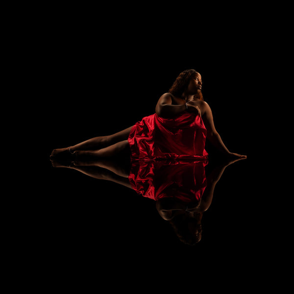 Low-key image capturing the essence of the Self-Love collection: a woman draped in red satin, her pose reflected on the surface below, creating a symmetrical expression of elegance and poise